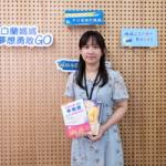 身穿花裙的女子站在品牌背景墙前，手里拿着两本彩色书
